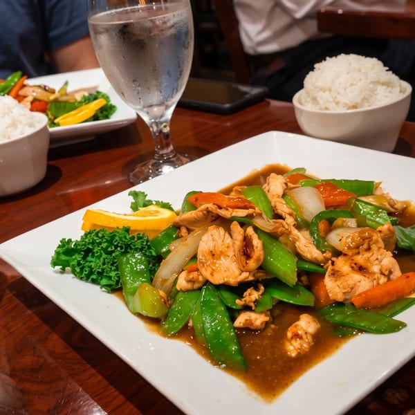 Chicken stir-fry with snow peas, bell peppers, and onions, served with rice and water glasses.
